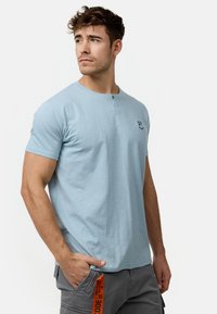 Svijetloplavi kratki rukav henley majica s dva gumba na izrezu, meke teksture i malim ispisanim logotipom na lijevoj strani prsnog koša.