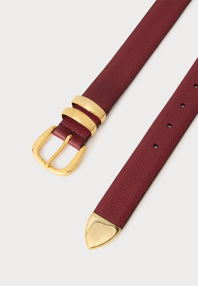 Ceinture en cuir rouge foncé avec boucle dorée, deux passants dorés et pointe dorée, posée à plat sur un fond clair.
