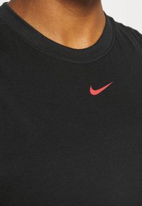 Zbliżenie na osobę w czarnej koszulce z małym czerwonym logo Nike w pobliżu obojczyka.