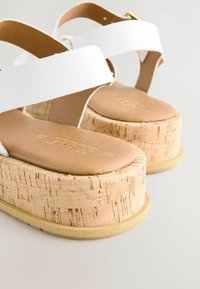 Sandales à plateforme blanches avec semelle en liège, semelle intérieure texturée marron et brides réglables. Remarquables pour leur design chunky et léger.
