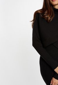 Maglione nero a coste con colletto alto e maniche lunghe, caratterizzato da un design a strati e una texture morbida.