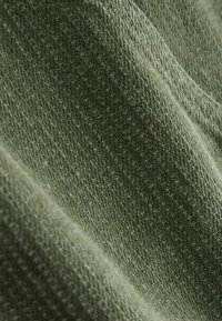 Texturált zöld szövet bordázott mintával, lágy matt felülettel és enyhe fényességgel, amely kötött szerkezetet jelez.