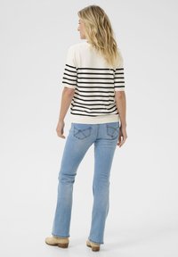 Maglietta a righe in crema e nero, abbinata a jeans svasati blu chiaro. La maglietta ha maniche corte e orlo a costine.