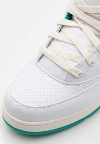 Białe skórzane sneakersy z perforowanym noskiem, kremowymi sznurówkami i turkusowymi akcentami na podeszwie. Gładka powierzchnia z teksturowanymi detalami.