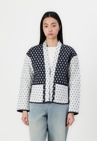 Quilted jacket featuring a navy and white geometric pattern, with a shawl collar, two front pockets, and a cropped design.