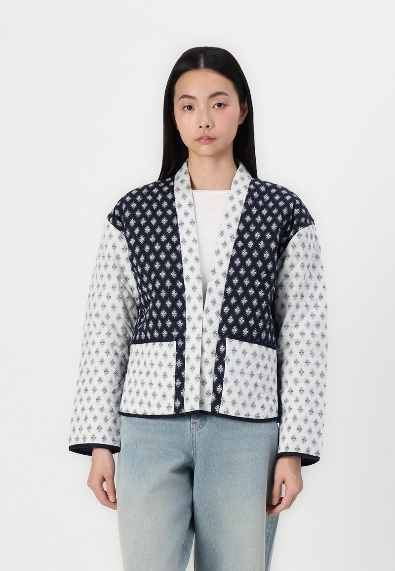 Quilted jacket featuring a navy and white geometric pattern, with a shawl collar, two front pockets, and a cropped design.