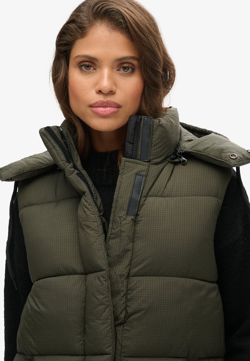 Grüße Pufferweste mit hohem Kragen, Reißverschlussfront und schwarzen Akzenten. Verfügt über ein gestepptes Muster und weiche Textur.