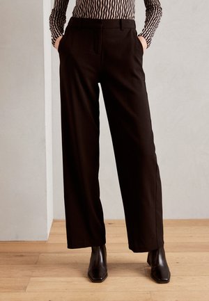 Pantalons noirs à jambe large avec une texture lisse, dotés de poches latérales et d'une coupe ajustée, associés à des bottines noires élégantes.