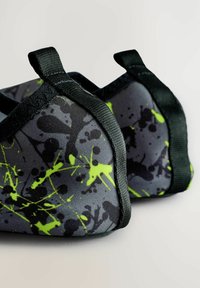 Fekete és szürke szövetcipő neon zöld fröccsenés mintával, masszív fekete szövetpántokkal a biztos illeszkedés érdekében és kerek formával.