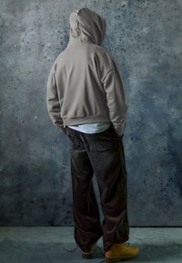 Felpa grigia con cappuccio e vestibilità ampia, abbinata a pantaloni neri di velluto a coste. L'outfit è completato da stivali da lavoro gialli ben evidenti.