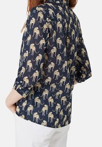 Chemise bleu marine avec imprimé léopard doré, manches longues retroussées, tissu léger, col boutonné et détail avec empiècement au dos.