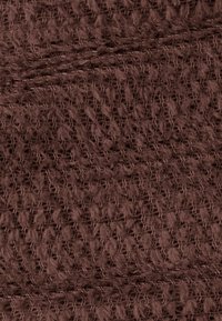 Brązowa dzianina z teksturowanym wzorem, zawierająca otwarte sploty i miękkie, puszyste nitki, tworząca ciepły, przytulny wygląd.