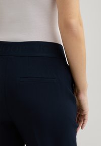 Dunkelmarinefarbene Hose mit breitem Bund, der den eingeprägten Markennamen trägt, und einer einzelnen Gesäßtasche, aus glattem Stoff mit taillierter Passform.