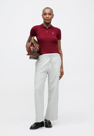 Burgundijas ribota polo krekls, pelēkas sporta bikses ar auklu un melni apavi. Modelis tur brūnu ādas soma. Vienkāršs, ikdienišķs apģērbs.