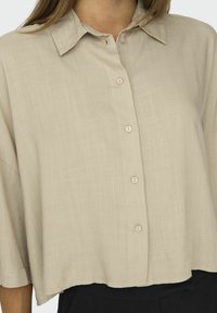 Beige kortærmet skjorte med knapper i blødt, tekstureret stof, med krave og fem forreste knapper, cropped nederste kant og afslappet pasform.