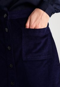 Námořnická kordová sukně s knofl�íkovým zapínáním, s boční nášivnou kapsou, texturovanou látkou a rovnými liniemi.