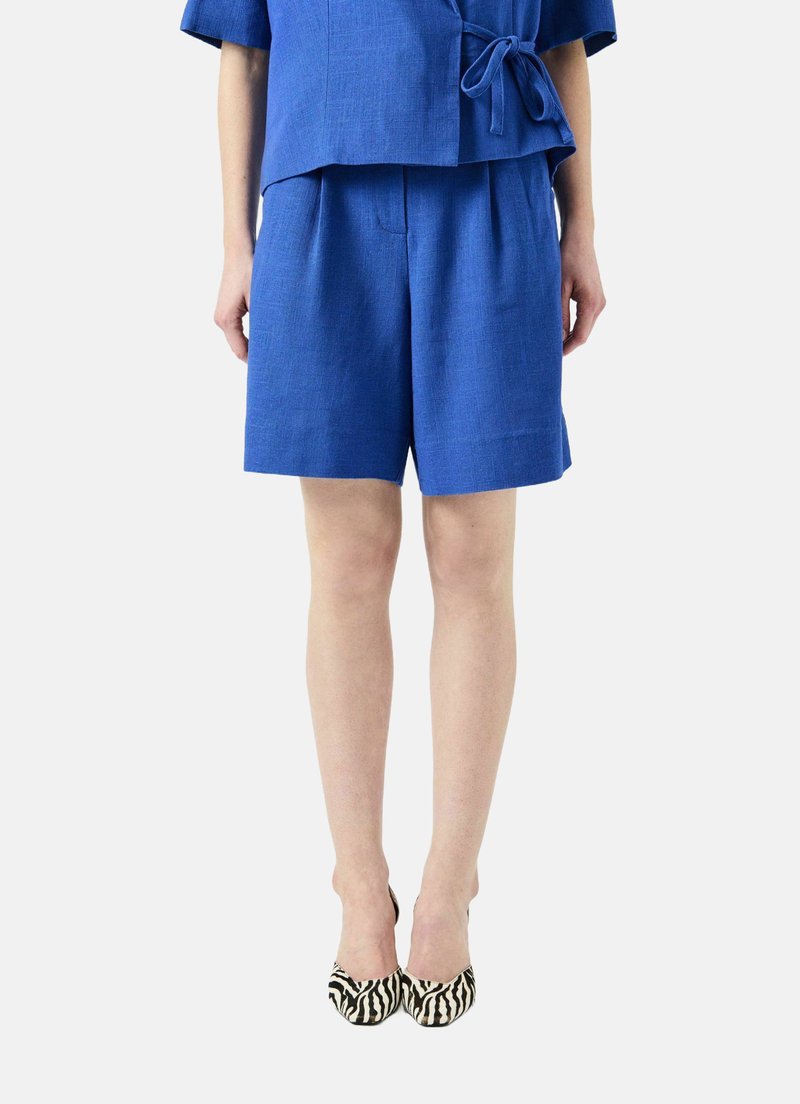 Modrý lněný dvoudílný outfit, který obsahuje krátký rukáv s páskem v oblasti pasu a šortky ke kolenům. Boty mají zebrovaný vzor.