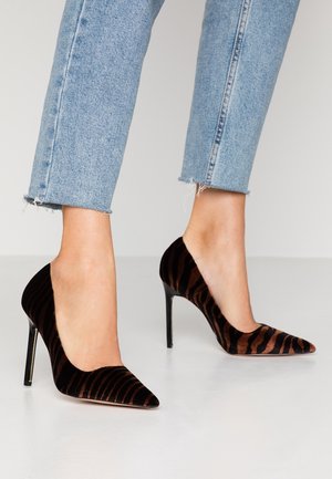 Zwart en bruin gestreepte fluwelen pumps met een puntige neus en stilettohak, gecombineerd met lichtblauwe jeans met rafelige zoom.