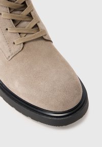 Stivale in suede beige con lacci piatti. Caratteristiche: punta rotonda e suola in gomma nera con dettagli testurizzati. Superficie liscia e leggera lucentezza.