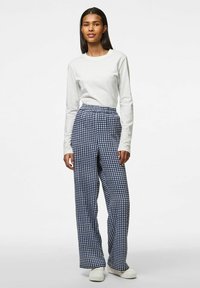 Vit långärmad skjorta ihop med högmidjade byxor i marinblå rutor, med en avslappnad passform och mjukt tyg, kompletterat med vita sneakers.