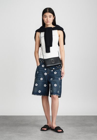 Shorts in denim con ricami floreali, abbinati a una canotta bianca e a un maglione nero di maglia appoggiato sulle spalle. Borsa a tracolla nera.