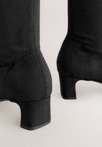 Bottes noires à la cheville en matière douce semblable au daim. Elles présentent un talon bloc, des détails de coutures et une texture lisse.