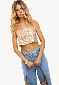 Geknipt top van iriserende pailletten in roze en gouden tinten. Gedragen met high-waisted blauwe spijkerbroeken en een gouden accessoiresriem.