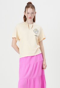 Light yellow cotton t-shirt with short sleeves and a flower graphic on the chest, paired with a tiered, textured pink skirt.