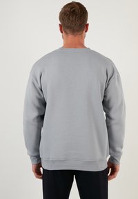 Sudadera gris con un corte relajado, puños y dobladillo de canalé, y diseño de cuello redondo. Textura suave, detalles mínimos y color sólido.