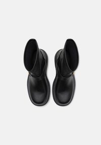 Botas de tobillo de cuero negro con una textura suave, punta redondeada y cremallera lateral. La suela exterior está ligeramente elevada y presenta un diseño minimalista.