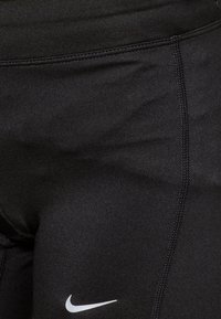 Leggings de sport noirs en tissu extensible, avec une coupe ajustée et des coutures plates, ornés d'un petit logo Nike blanc sur le côté gauche.