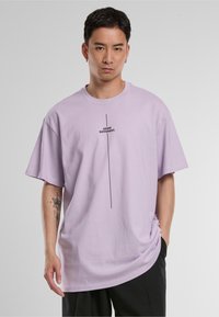 Lilac oversized t-shirt with short sleeves, featuring a central black print saying "I THINK DIFFERENT." Smooth cotton texture.