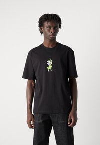 Camiseta de algodón negra con mangas cortas que presenta un colorido estampado gráfico de dinosaurio centrado en el pecho. Diseño simple y sin adornos.