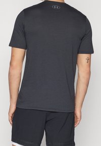 Mörkgrå kortärmad träningsskjorta i lättviktsmaterial, med en subtil logotyp på övre delen av ryggen och rund halsringning.