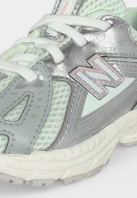 Κοντινή λήψη αθλητικού παπουτσιού New Balance σε ασημί και ανοιχτό πράσινο με λευκά κορδόνια και υφασμάτινη, υφή με δίχτυ.