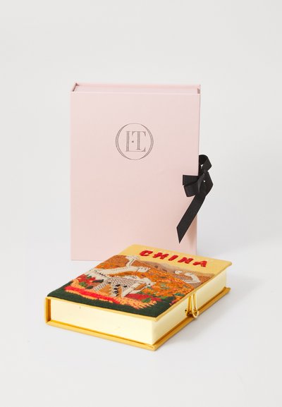 Livre jaune intitulé "Chine" avec une couverture brodée représentant des paysages et des bâtiments, posé à côté d'une boîte rose avec un ruban noir.