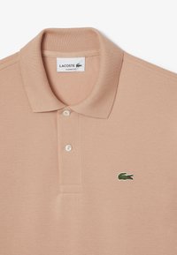 Camisa polo de color rosa claro con un tejido texturizado, que presenta un cuello clásico, una tapeta de tres botones y un logotipo de cocodrilo verde bordado.