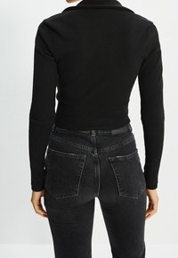 Maglietta nera a maniche lunghe con texture a coste; design aderente. Abbinata a jeans neri a vita alta con tasche posteriori.