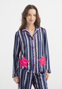 Marine gestreepte pyjamastel met roze zigzagpatronen, met grote roze ster applicaties op de zakken en rode afwerking op de kraag en knopen.