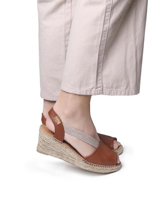 Brown leather wedge sandals with open toe, elastic ankle strap, and woven jute sole. Features a smooth texture and minimalistic design.