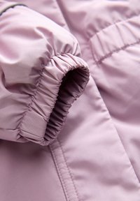 Gros plan sur une manche de veste violet clair avec poignet élastique et détails de coutures sur tissu lisse.