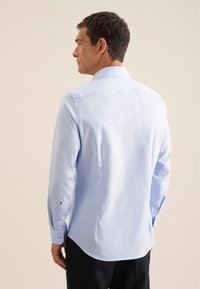 Lichtblauw langemouwen shirt van gladde stof, met een klassieke kraag, rugplooi en met knopen afgewerkte manchetten. Het ontwerp is getaillede en aansluitende.
