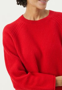 Pull en tricot rouge avec une texture côtelée, col rond et manches longues, présentant des épaules raglan pour un fit décontracté.