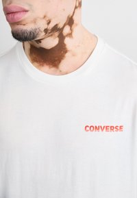 White cotton t-shirt featuring a small red "CONVERSE" logo on the chest, with a round neckline and short sleeves.