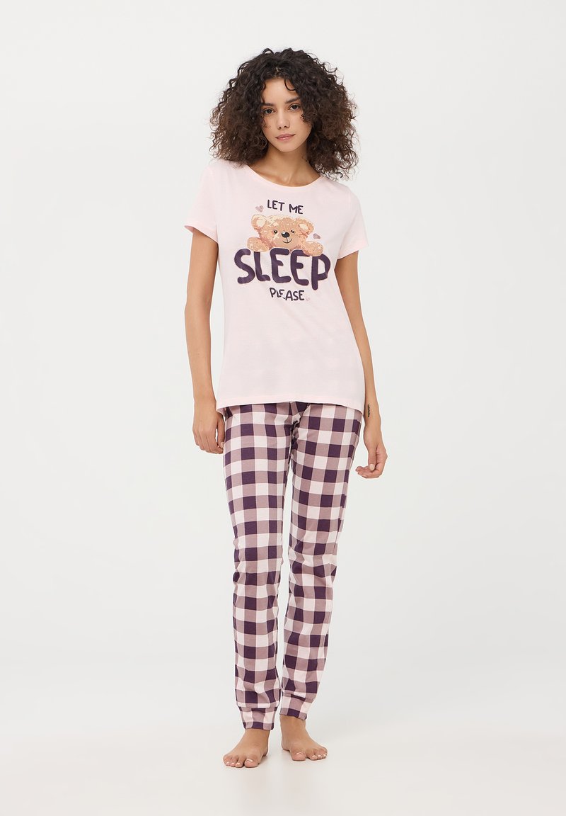 T-shirt in cotone rosa chiaro con la scritta "Per favore, lasciami dormire" e una grafica di un orsetto. Pantaloni da pigiama a scacchi viola e bianchi in tessuto morbido.