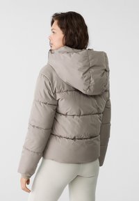 Svetlo šedá puff jacket s kapucňou, so prešívaným dizajnom a elastickými manžetami. Hladká textúra a mierne priliehavý strih.