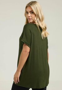 Camiseta de corte oversize en verde oliva, confeccionada en tejido suave, con mangas cortas enrolladas, un ajuste relajado y un dobladillo recto.