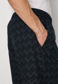 Shorts de sport bleu marine avec une taille élastique et des poches latérales, présentant un motif géométrique noir subtil et texturé.