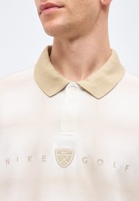 Άνδρας με ανοιχτό μπεζ πόλο μπλούζα Nike Golf με μπεζ γιακά και κεντημένο λογότυπο στο στήθος.
