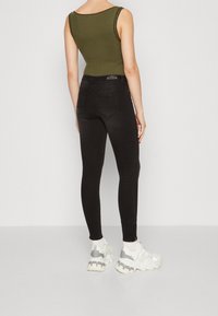 Bodysuit de canalé en verde olivo combinado con jeans negros ajustados. Los jeans tienen bolsillos traseros y una silueta skinny. El modelo lleva unas zapatillas blancas gruesas.